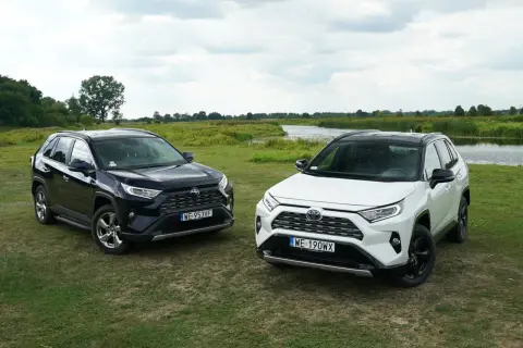Dwa nowe modele Toyota RAV4 2025, czarny i biały, zaparkowane na trawie nad jeziorem.