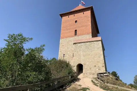 Wieża zamku Melsztyn z polską flagą na szczycie, kamienna podstawa i ceglana nadbudowa.