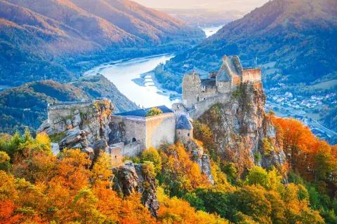 Zamek na skale w dolinie Wachau, otoczony jesiennymi barwami, z rzeką w tle.