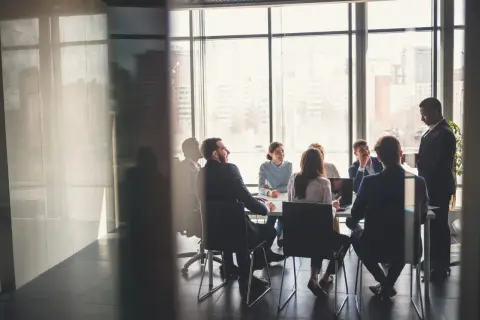 Grupa ludzi w garniturach podczas walnego zgromadzenia w sali konferencyjnej z widokiem na miasto.