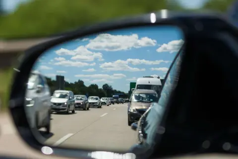 Autofahrer stellt den spiegel richtig ein, um den Verkehr auf der Autobahn zu sehen. Blauer Himmel mit Wolken spiegelt sich im Spiegel.