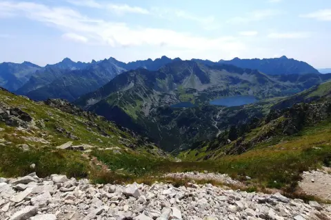 Widok z przełęczy na skraju Orlej Perci na Tatry Wysokie. Dwa jeziora w dolinie, skaliste zbocza i szczyty w oddali.