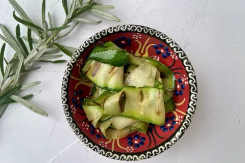 Gegrillte Zucchinibänder in einer bunten Schale, daneben Rosmarin. Perfekt, um zu sehen, was passt zu Zucchini!