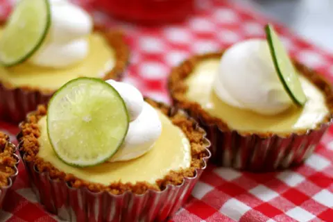 Små key lime pies med vispad grädde och limeklyfta på en rödvitrutig duk.