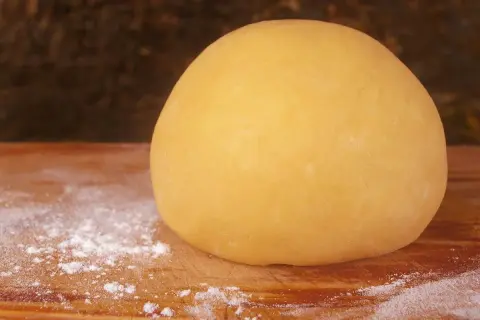 Impasto di pasta frolla per pastiera, 1 kg, pronto per essere steso su un tagliere infarinato.