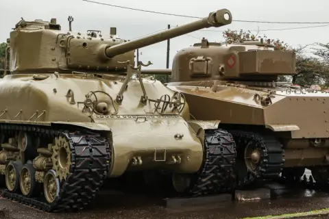 Dwa czołgi Sherman, których kraj pochodzenia to USA, stoją obok siebie na mokrej nawierzchni.