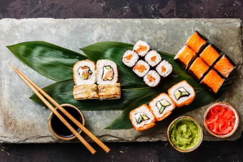 Sushi-Platte mit Lachs-Rollen, Nigiri und Beilagen. So isst man Sushi richtig: mit Stäbchen, Sojasauce, Wasabi und eingelegtem Ingwer.