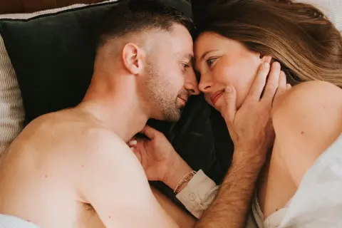 Un couple se regarde tendrement au lit. Ils semblent se retrouver après une période difficile, peut-être après une naissance et une épisiotomie, redécouvrant l'intimité.