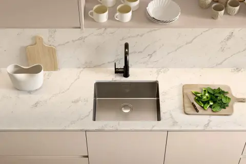 Plan de travail cuisine avec un évier en inox, un robinet noir, une planche à découper en bois avec des poivrons verts et des épinards, et une autre planche en bois.