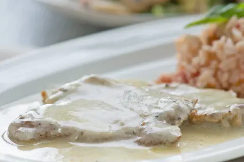Zartes Putenschnitzel mit cremiger Rahmsauce, serviert mit einer Beilage aus Reis. Ein köstliches Gericht.