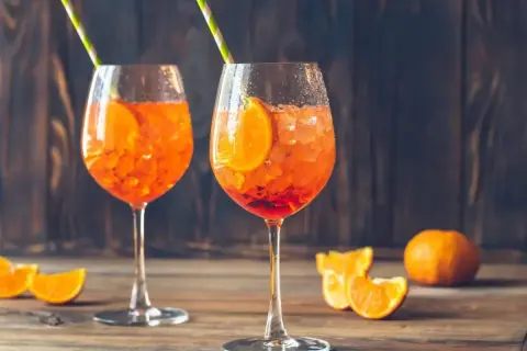 Dwa orzeźwiające drinki orange spritz z plasterkami pomarańczy i słomkami, na drewnianym stole.