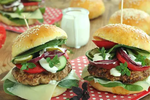 Dwa domowe burgery z serem, warzywami i sosem na drewnianym tle.