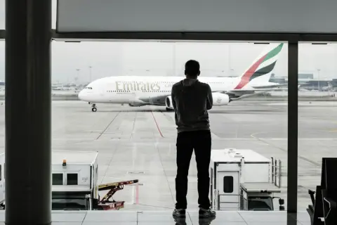 Mężczyzna w bluzie patrzy na samolot Emirates. Czeka na swój bagaż podręczny.
