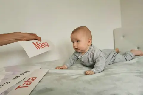 Uroczy noworodek na brzuchu, zaciekawiony kartkami z napisami "Mama" i "Tata".