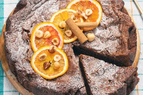 Torta di pane ricetta della nonna, cosparsa di zucchero a velo, decorata con fette d'arancia, nocciole e cannella.