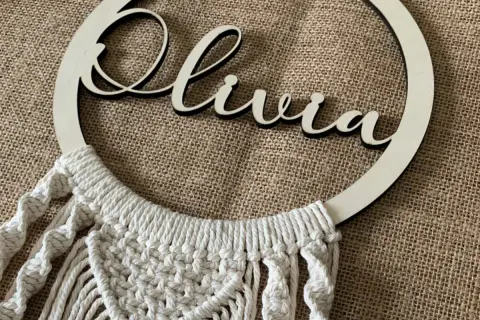 Un bel attrape-rêve personnalisé pour fabriquer un attrape rêve avec prénom. Le prénom "Olivia" est inscrit en lettres de bois sur un cercle orné de macramé.