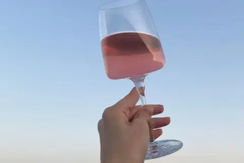 Różowe letnie wino w kieliszku, unoszone na tle błękitnego nieba. Idealny moment na orzeźwienie.
