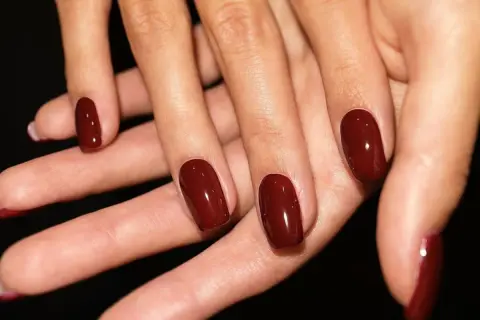 Dłonie z idealnie pomalowanymi na głęboki, wiśniowy kolor paznokciami. To zdecydowanie trendy paznokcie wiosenne, które dodają elegancji.