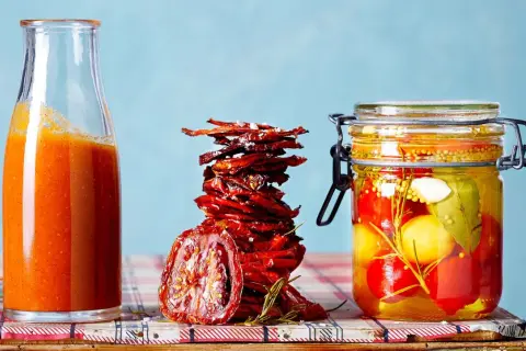 Glas mit eingelegten Tomaten, daneben ein Stapel sonnengetrockneter Tomaten und eine Flasche Tomatensauce.