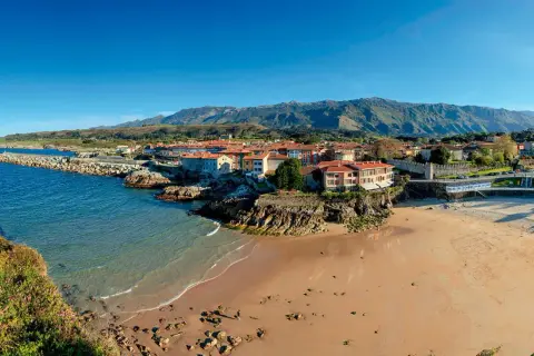 Costa asturiana con playa, pueblo costero y montañas. Descubre qué ver en Nueva de Llanes, un paraíso natural.