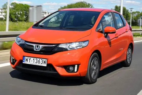 Pomarańczowy Honda Jazz w ruchu drogowym. Wiele osób szuka honda jazz opinie przed zakupem.
