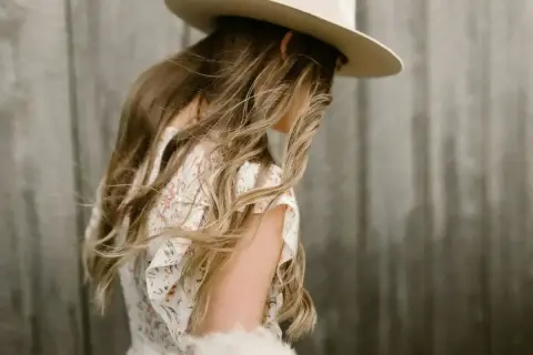 Kobieca stylizacja na wesele w stylu boho: zwiewna sukienka w kwiaty, kapelusz i delikatne dodatki.