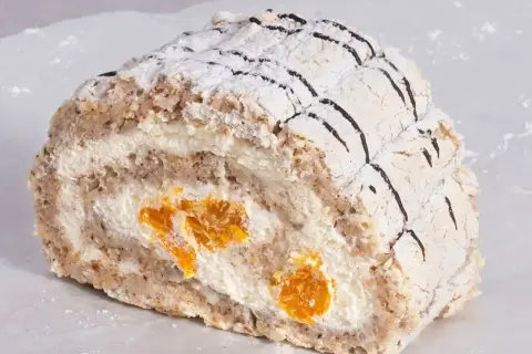 En bit Budapest bakelse med vispgrädde och aprikoser, pudrad med florsocker och dekorerad med choklad.
