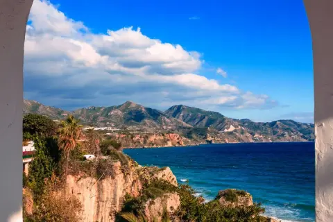 Vue panoramique de la côte andalouse, parfaite pour un guide Malaga. Falaises rocheuses, mer bleue et montagnes verdoyantes sous un ciel d'azur.