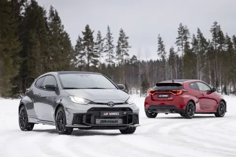 Dwa sportowe toyoty hatchback GR Yaris na śniegu, jeden szary z przodu, drugi czerwony z tyłu, na tle zimowego lasu.