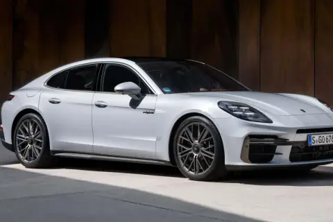 Elegancki, biały Porsche Panamera 2024 z czarnym dachem i przyciemnianymi szybami, zaparkowany na tle rustykalnej ściany.