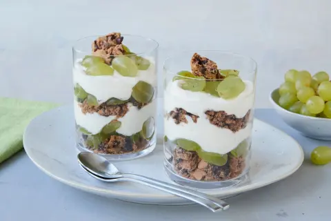 Zwei Gläser mit einem leckeren Trauben-Cookie-Dessert, geschichtet mit Joghurt und Keksbröseln.