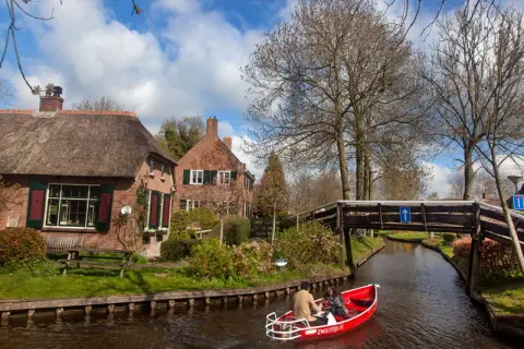 Paseo en barca por los canales de Giethoorn, Holanda, con casas de tejado de paja y un puente de madera.