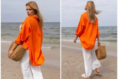 Kobieta w pomarańczowej koszuli i białych spodniach na plaży. Idealne outfity na lato, z plecioną torbą.