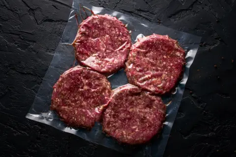 Cztery surowe kotlety na hamburgery w folii. Zastanawiasz się, mięso na hamburgery jak przyprawić?