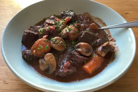 En mustig boeuf bourguignon med möra köttbitar, champinjoner och morötter i en djup rödvinssås, toppad med persilja.