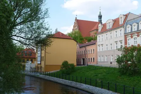Nad rzeką malownicze kamienice. Chcesz wiedzieć, jak sprawdzić czy budynek jest w rejestrze zabytków? Spójrz na detale architektoniczne i wieżę kościelną.