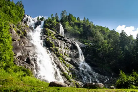 Le Cascate Nardis, un imponente salto d'acqua che scende su rocce scure, circondate da un verde lussureggiante e alberi imponenti sotto un cielo azzurro.