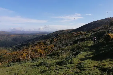 Senderismo en el monte Seixo, con molinos de viento en la cima y un valle verde al fondo.