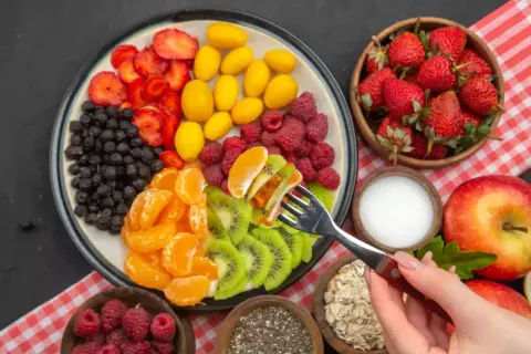Kolorowa uczta dla ciała: truskawki, borówki, maliny, kumkwaty, kiwi i mandarynki. Idealna dieta warzywno owocowa na talerzu.