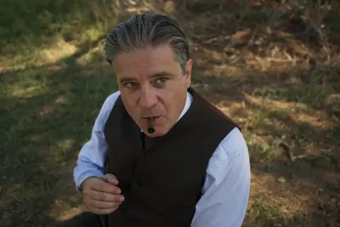 Un uomo con un sigaro in bocca, vestito elegantemente, sembra un re.