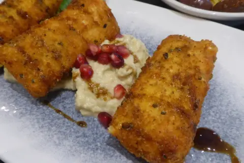 Złociste, panierowane kawałki halloumi, idealnie usmażone, podane z kremowym hummusem i granatem. Warto wiedzieć, ile smażyć halloumi, by uzyskać taki efekt.
