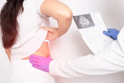 Lekarz w niebieskiej rękawiczce trzyma wyniki badań, podczas gdy pacjentka w białej koszulce odsłania bok. To ilustracja, jak wygląda badanie urologiczne u mężczyzn.
