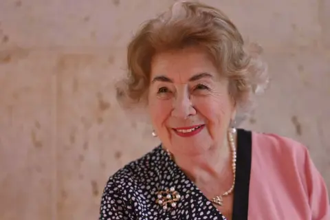 Lächelnde ältere Dame mit Perlenkette und Brosche, die eine positive Ausstrahlung hat, trotz möglicher maria prean kritik.