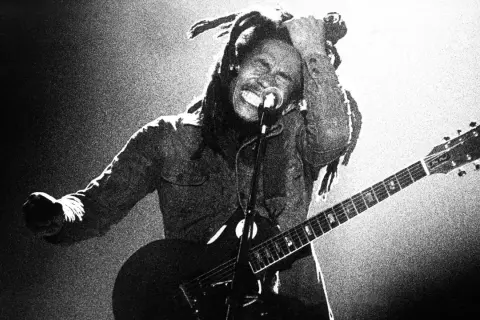 Bob Marley z gitarą, w transie, śpiewa na scenie. Jego dredy unoszą się w powietrzu, a ręka sięga do głowy. To ikona muzyki, której rytmy ska porwały tłumy.