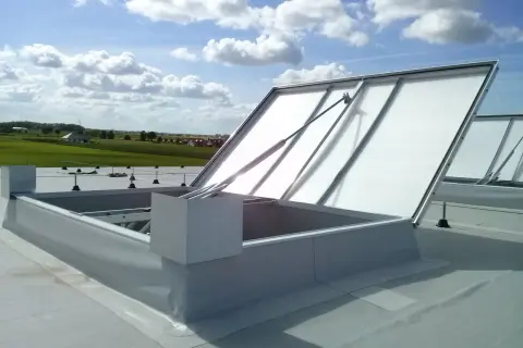 Otwarta klapa dymowa na dachu, z widokiem na zielone pola i błękitne niebo z chmurami.