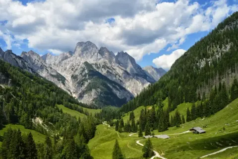 Grüne Almwiesen und Nadelwälder schlängeln sich zu majestätischen Berggipfeln. Kleine Hütten und Pfade deuten auf Berchtesgaden Geheimtipps hin.