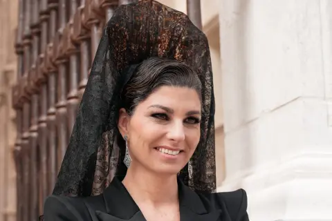 Mujer con peinado boda gitana, velo de encaje negro y pendientes largos. Sonríe con elegancia.