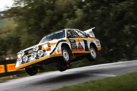 Klasyczny Audi Sport Quattro w akcji, unoszący się nad zakrętem. Ikona rajdów.