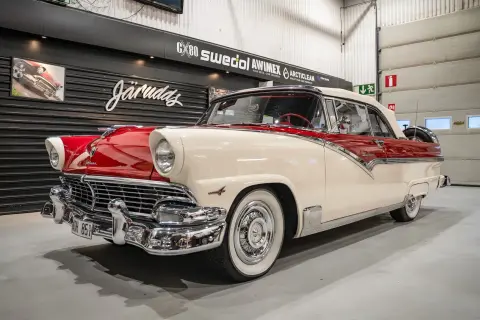 En skinande röd och vit Ford 56 cabriolet står i ett garage.