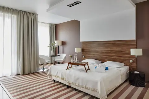 Przytulny pokój hotelowy z dwoma łóżkami, stolikiem i fotelami, ozdobiony drewnianym zagłówkiem i pasiastym dywanem.
